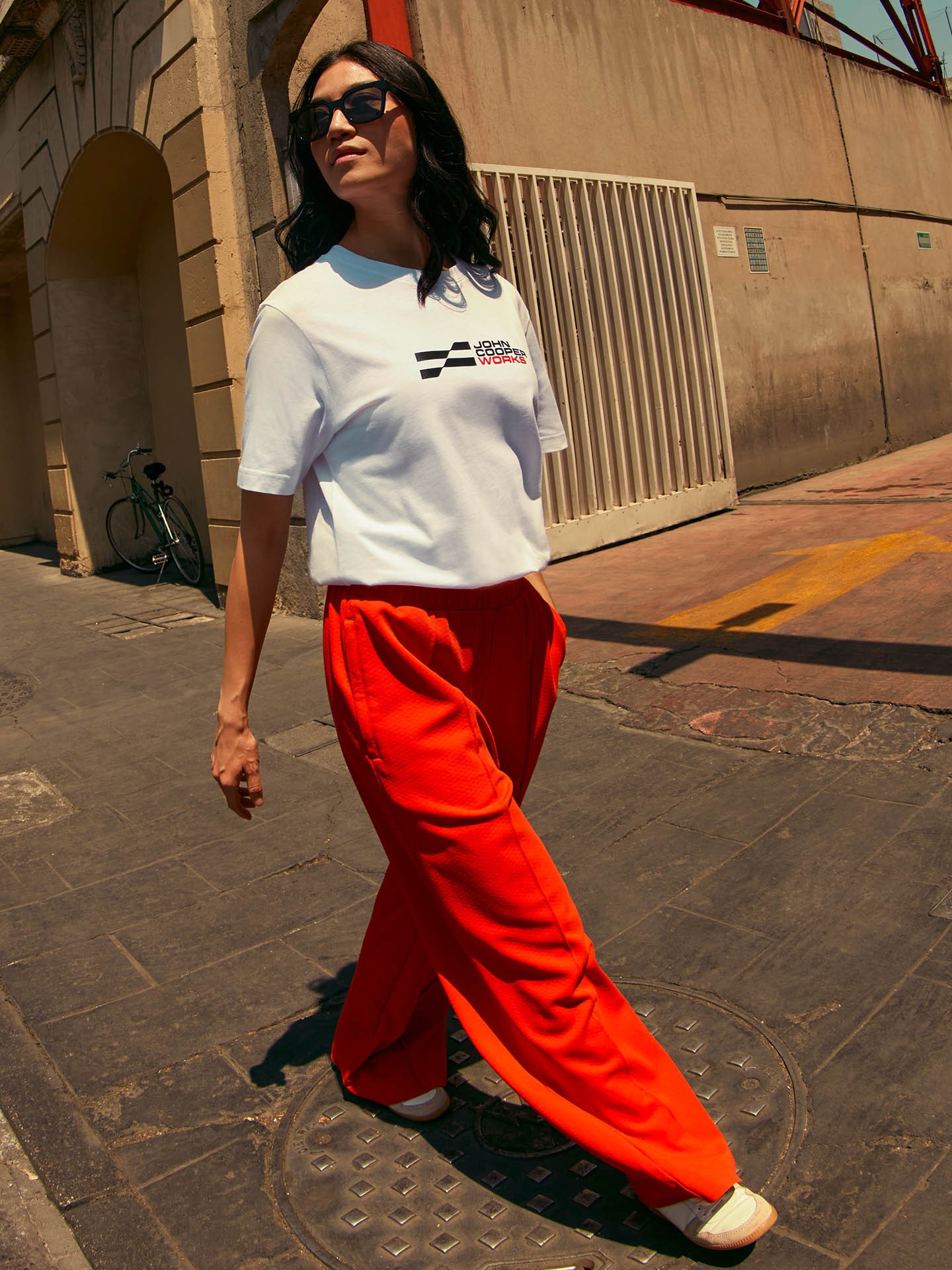 Female model wears white JCW t-shirt and red pants